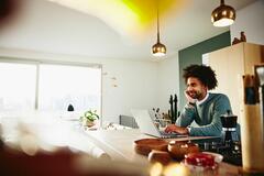 Man leaning against the counter top, while working on laptop.