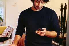 Man standing next to the kitchen counter top, looking at his phone.