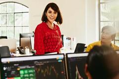 Smiling woman talking to colleagues, standing between desks.