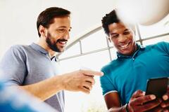 Two smiling colleagues (men) looking at a phone.