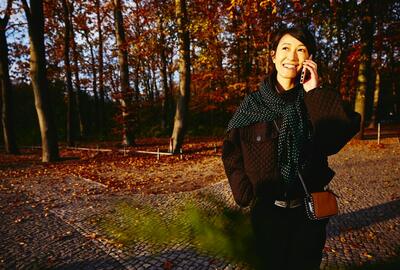 Smiling woman on the phone, autumn trees on background.