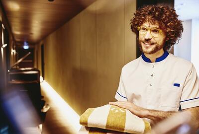 Man in uniform holding towels in a hallway of a hotel.