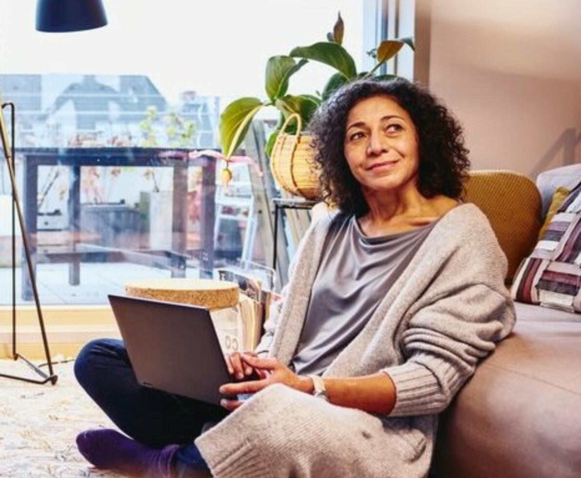 Woman leaning against a couch, sitting on the floor, with laptop on her lap