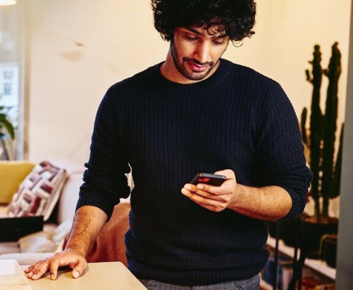 Man standing next to the kitchen counter top, looking at his phone.