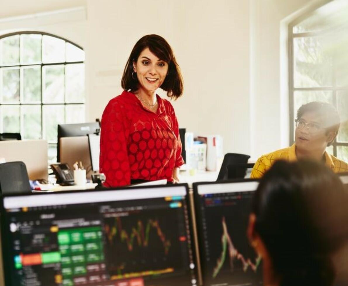 Smiling woman talking to colleagues, standing between desks.