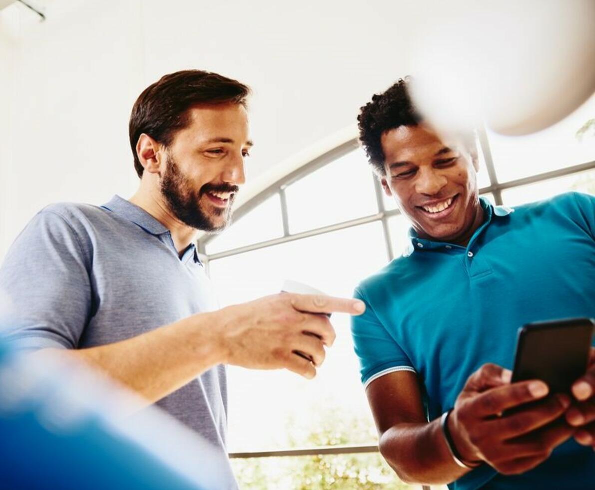 Two smiling colleagues (men) looking at a phone.