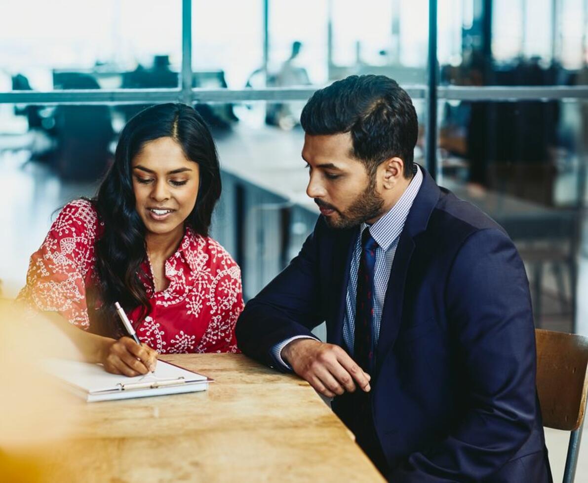 India Woman and man working together sitting at a table and taking notes.