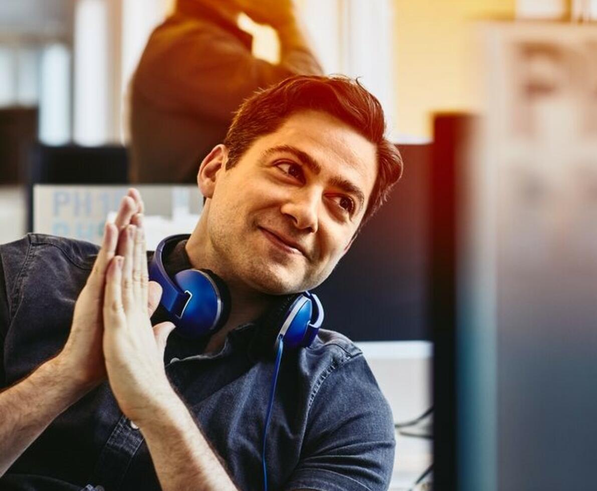 Smiling man with headphones having a conversation at his desk.