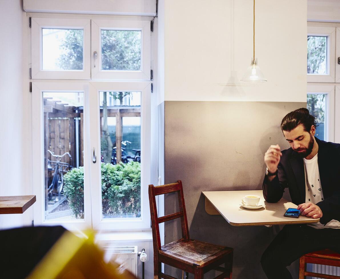 Man sitting at table with a coffee, looking seriously at his phone.