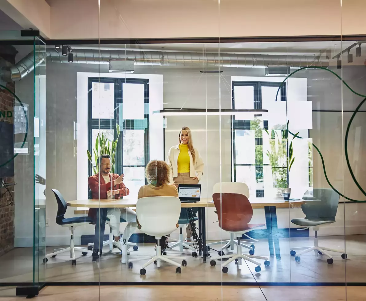 Female and male are sitting and female is standing at a table in a office meeting room