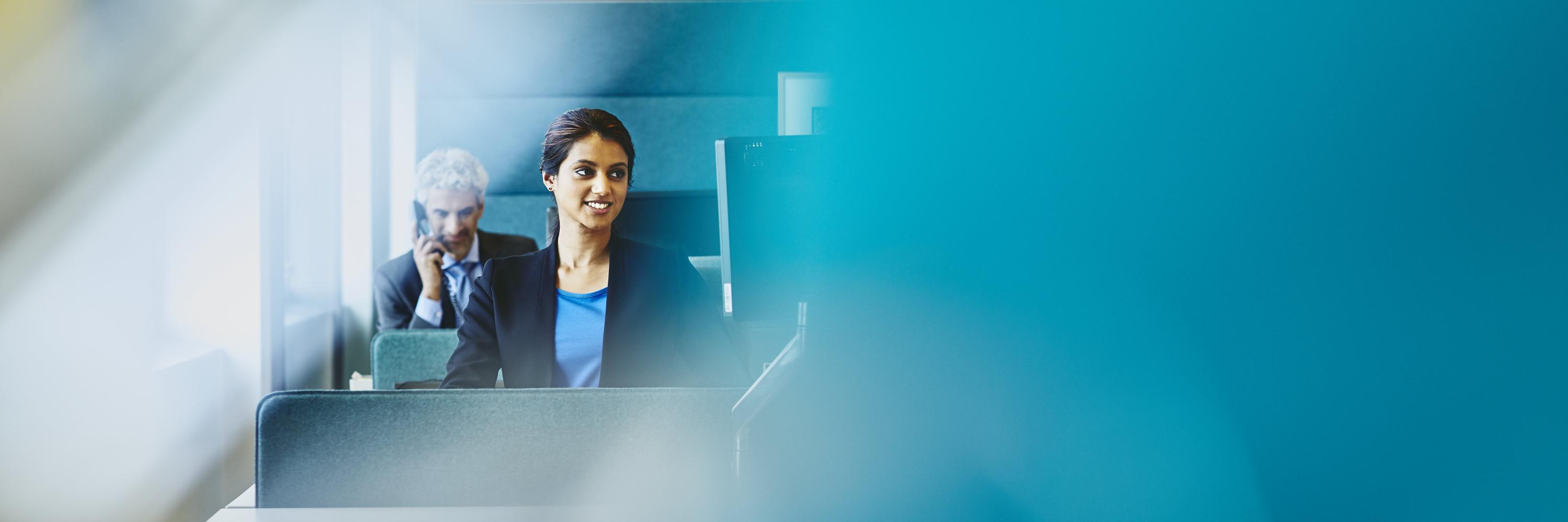 Woman working in her cubicle. Man calling. India. Primary color: blue.