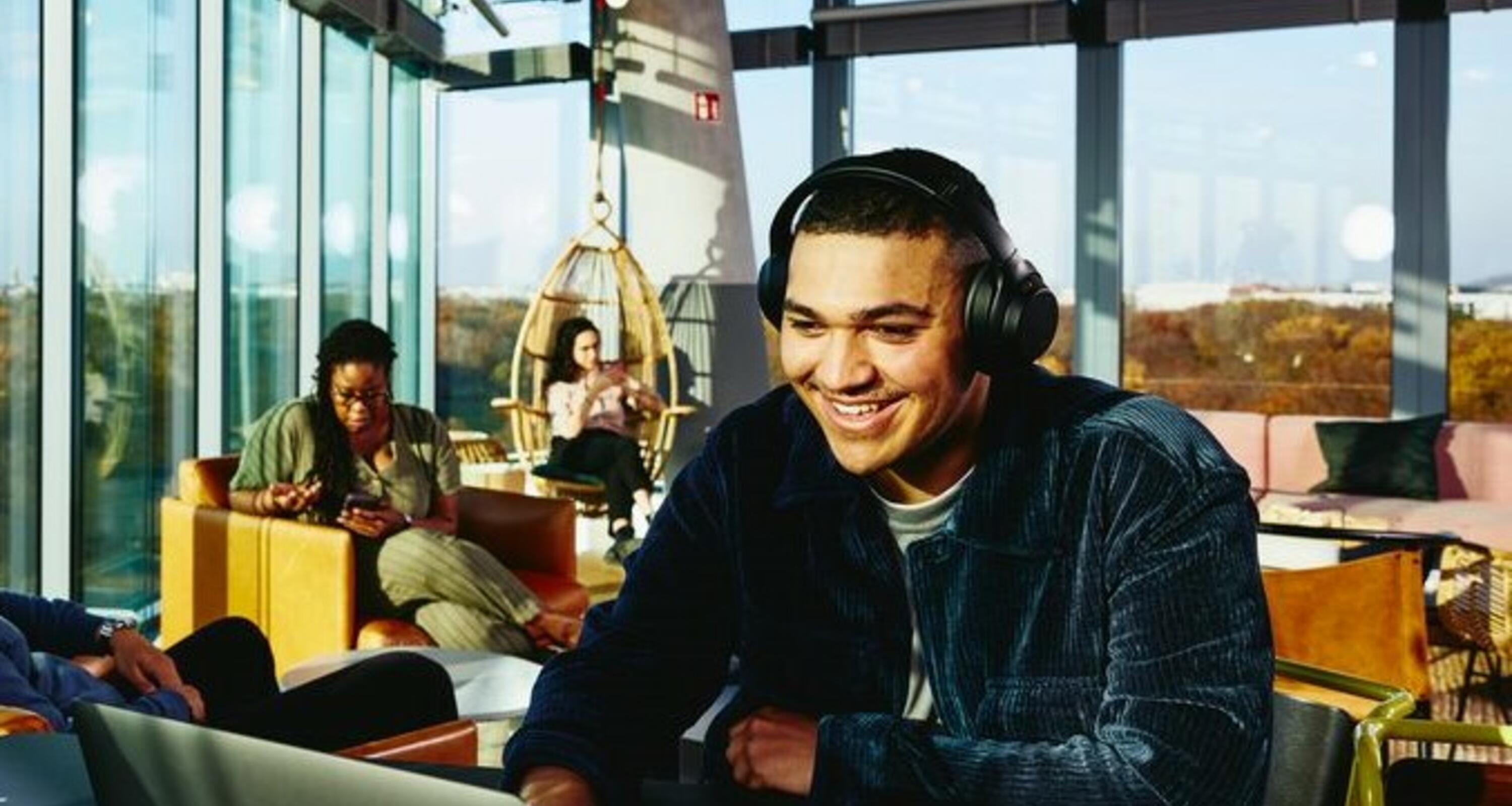 Smiling man with headphones and laptop sitting in a lounge environment.