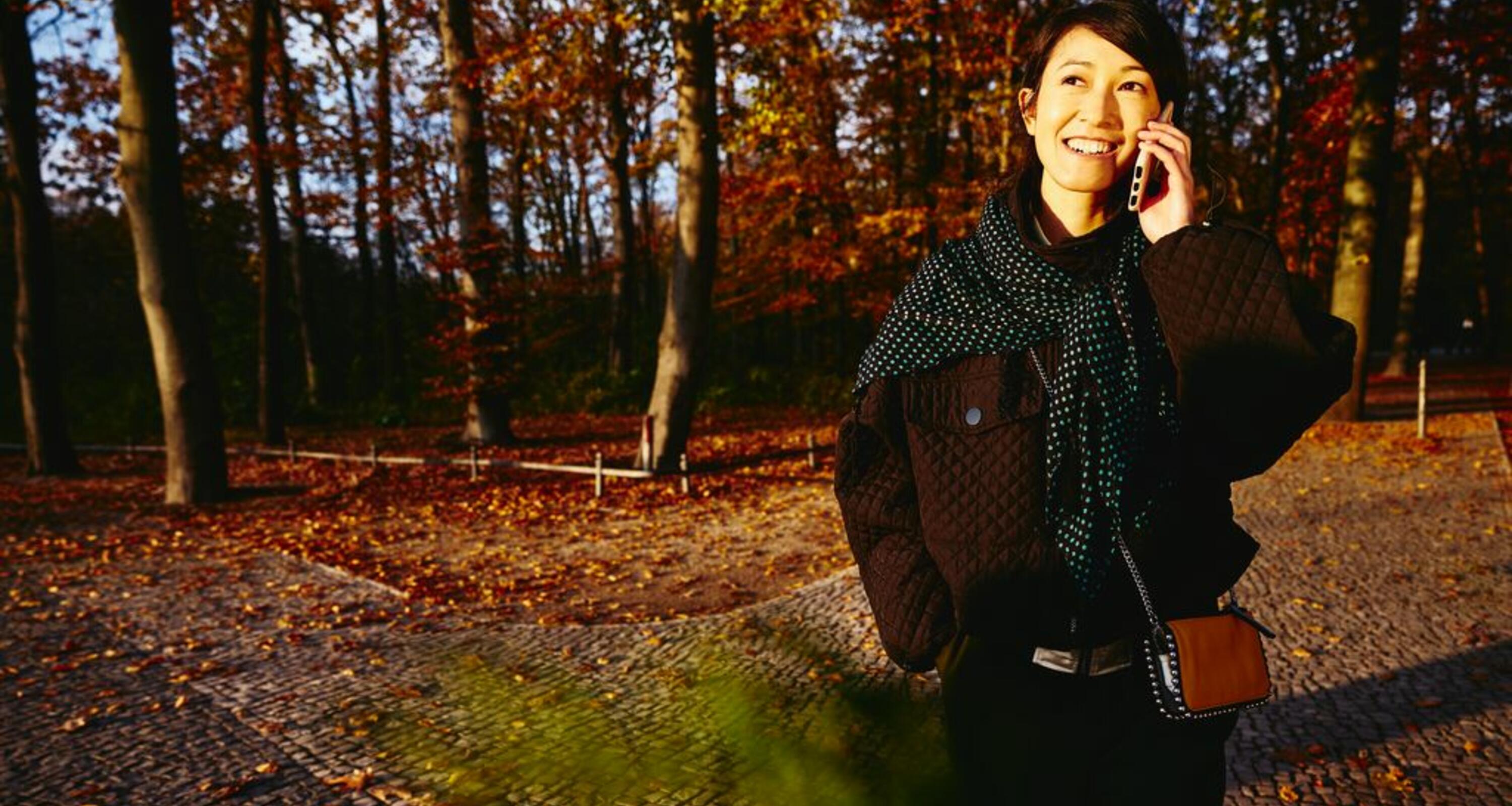 Smiling woman on the phone, autumn trees on background.