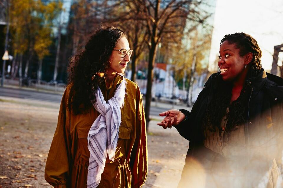 Two woman walking outside while having a conversation, smiling.