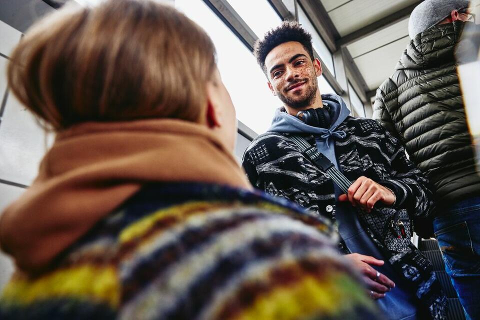 Smiling man standing backwards on escalator looking at a woman at a train station.