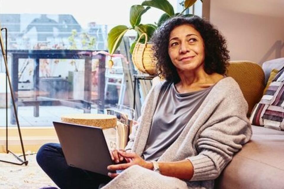 Woman leaning against a couch, sitting on the floor, with laptop on her lap