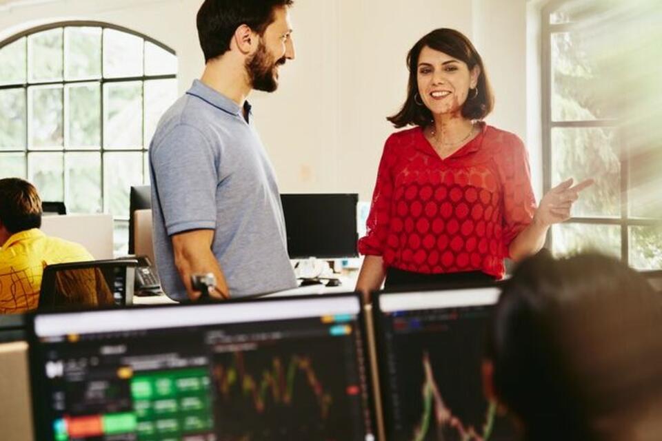 Two colleagues man and woman having a chat standing between desks.