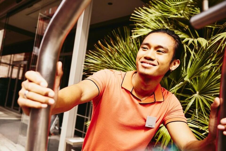 Smiling bellhop pushing a luggage trolley outside a hotel entrance.