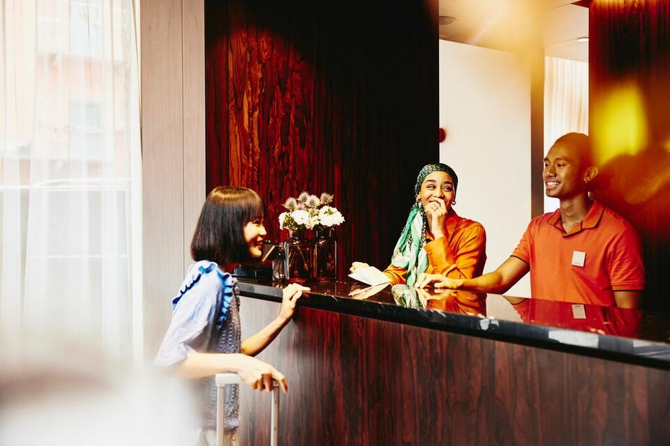 Smiling man and woman working at a hotel reception desk helping a guest.