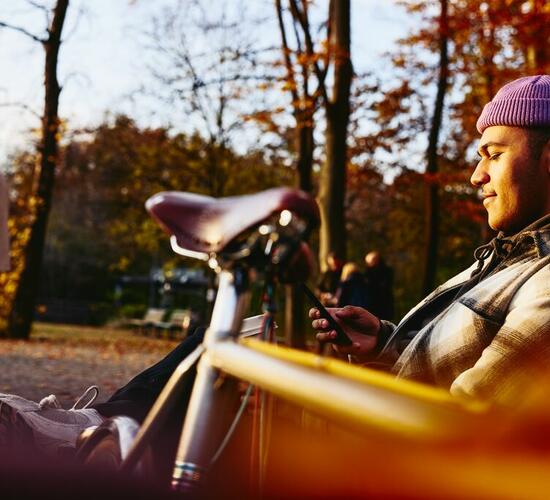 Man sitting on a bench with his bike next to him, looking at his phone.