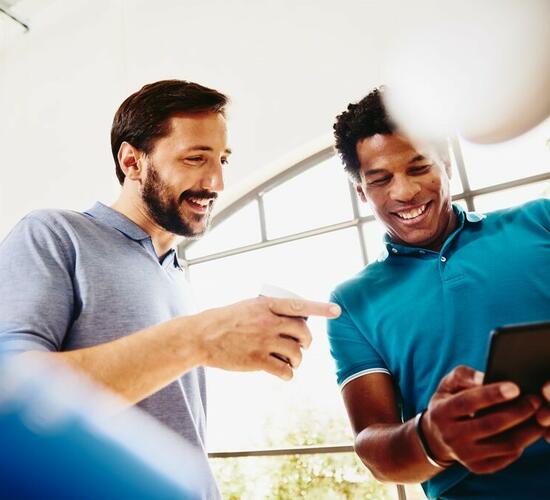 Two smiling colleagues (men) looking at a phone.