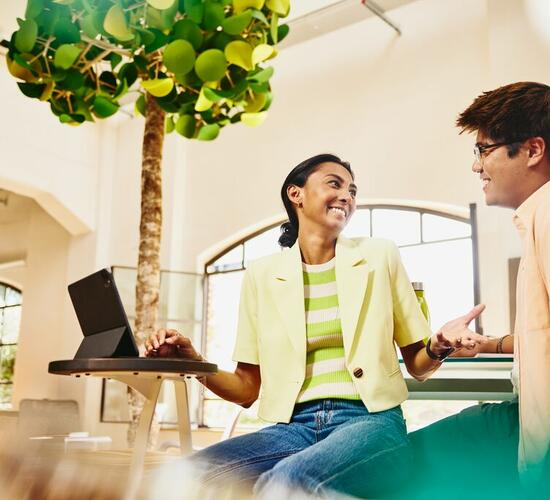 Man and woman sitting at table having a chat, while woman working on a tablet.