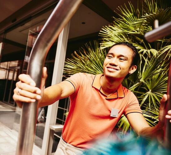 Smiling bellhop pushing a luggage trolley outside a hotel entrance.