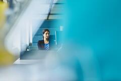 Woman working in her cubicle, looking at her desktop computer. India. Primary color: blue.