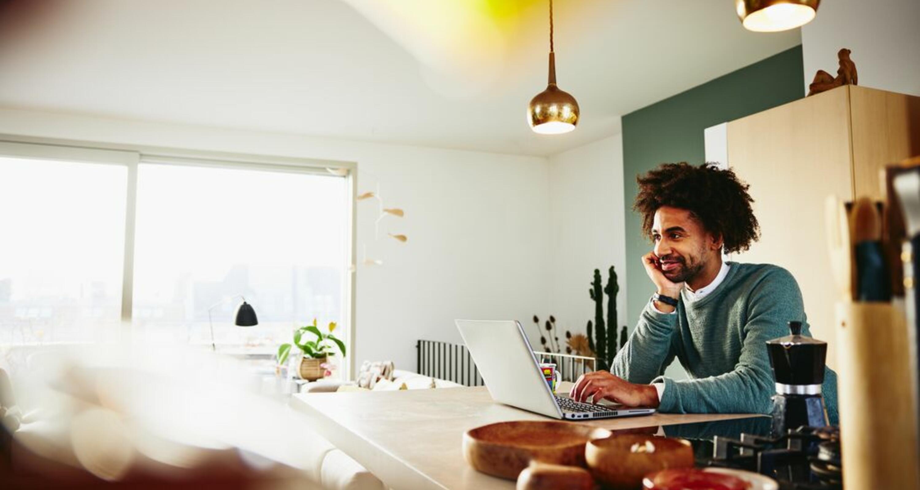 Man leaning against the counter top, while working on laptop.